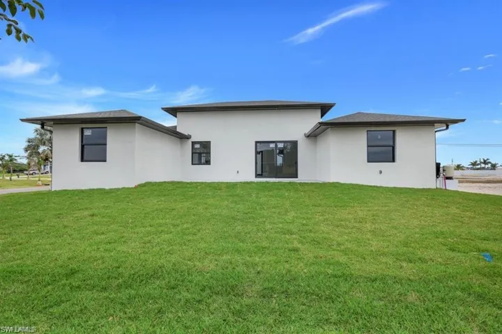 Rear view of house featuring stucco siding and a lawn