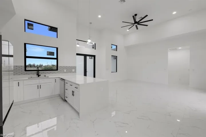 Kitchen featuring open floor plan, dishwasher, light marble finish flooring, a peninsula, and light countertops