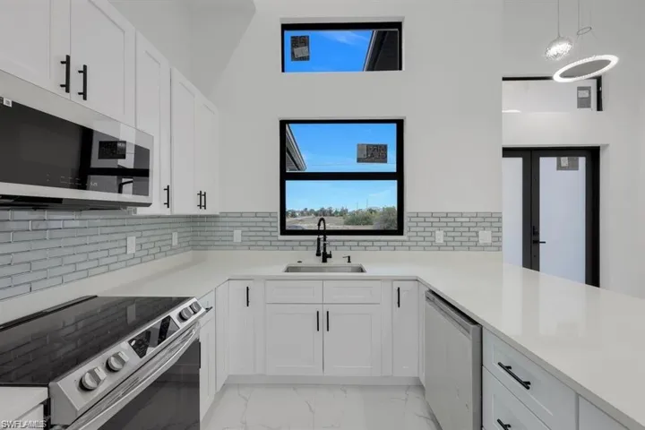 Kitchen featuring appliances with stainless steel finishes, light marble finish floors, white cabinetry, light countertops, and decorative backsplash