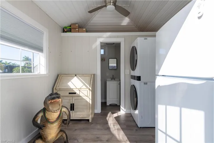 Laundry area featuring a ceiling fan, stacked washer and dryer, dark wood-type flooring, and wood ceiling