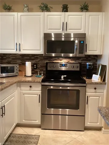 Kitchen with white cabinetry, backsplash, stove, light tile patterned floors, and light stone counters