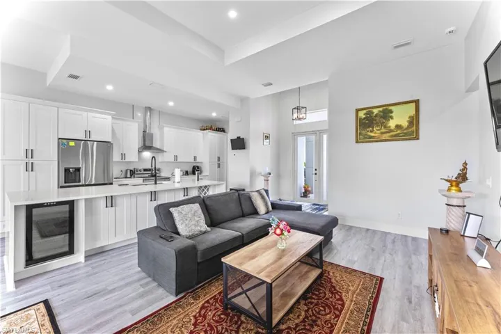 Living room with wine cooler, sink, light hardwood / wood-style floors, and a raised ceiling