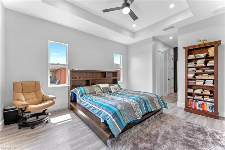 Bedroom with ceiling fan, a raised ceiling, light hardwood / wood-style floors, and multiple windows