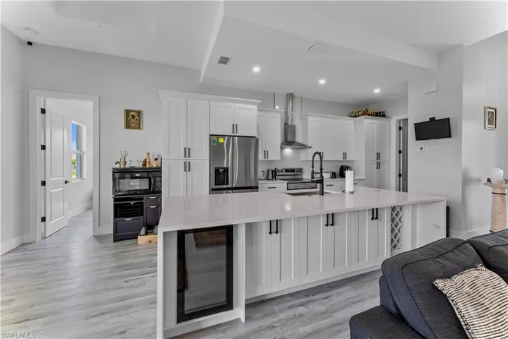 Kitchen featuring wall chimney range hood, light hardwood / wood-style flooring, appliances with stainless steel finishes, white cabinets, and a large island