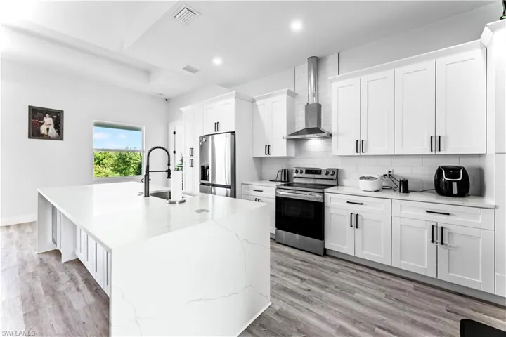 Kitchen with wall chimney range hood, light hardwood / wood-style flooring, a kitchen island with sink, and appliances with stainless steel finishes