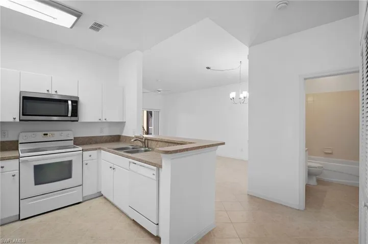 Kitchen featuring white appliances, white cabinetry, a peninsula, ceiling fan, and a chandelier