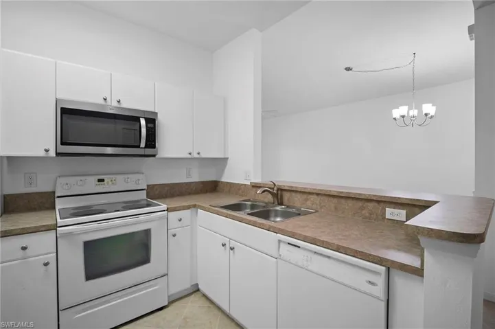 Kitchen with white appliances, a peninsula, white cabinetry, hanging lights, and light tile patterned floors