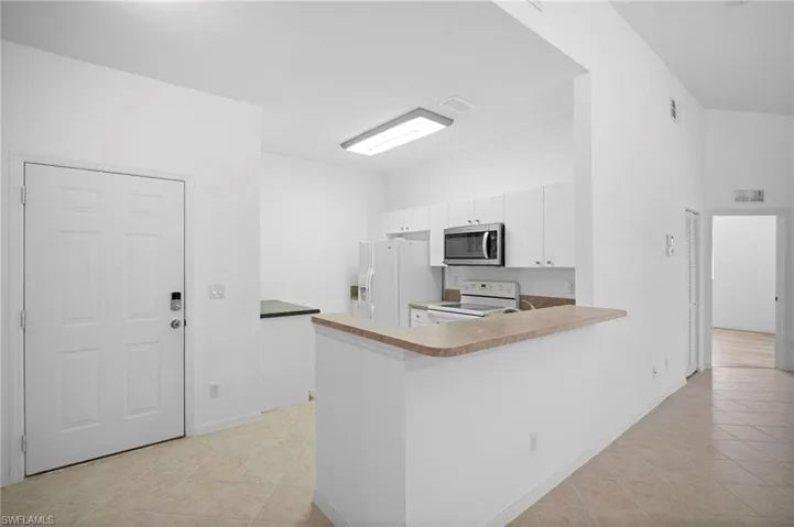 Kitchen featuring white cabinets, a peninsula, white range with electric cooktop, stainless steel microwave, and light tile patterned flooring