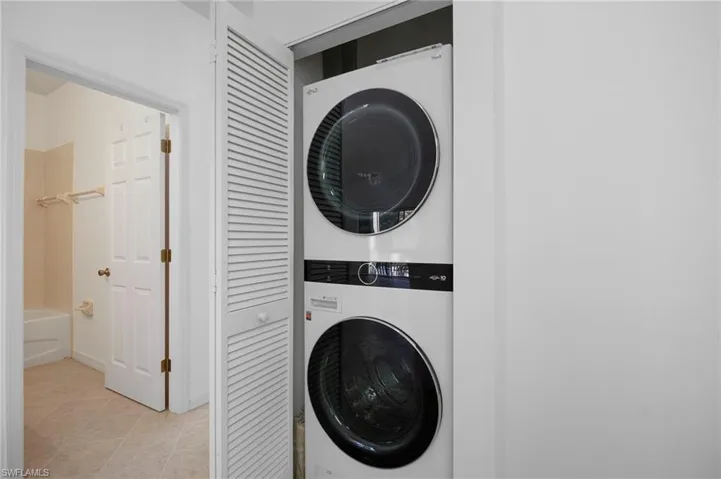 Laundry area with stacked washer and clothes dryer and light tile patterned flooring
