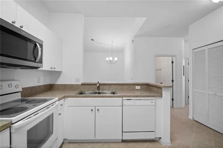 Kitchen featuring white appliances, a peninsula, white cabinets, and hanging lights