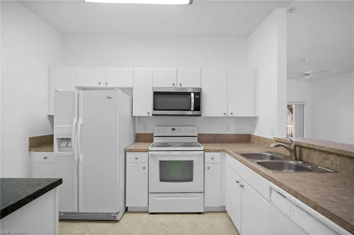 Kitchen featuring white appliances, white cabinetry, and ceiling fan