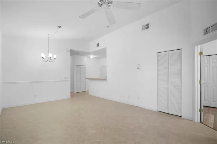 Unfurnished living room with a ceiling fan, a chandelier, and a high ceiling