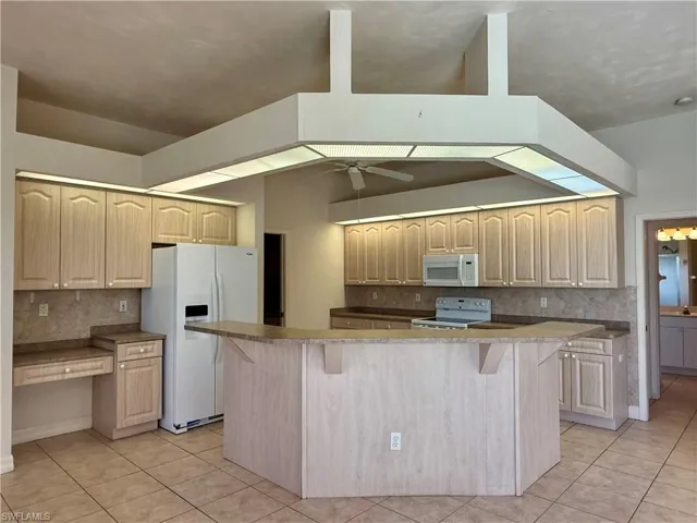 Kitchen featuring a breakfast bar, light brown cabinets, white appliances, and tasteful backsplash.