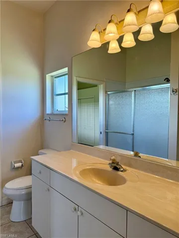Jack and Jill Bathroom featuring toilet, tile patterned floors, a shower with shower door, and vanity.