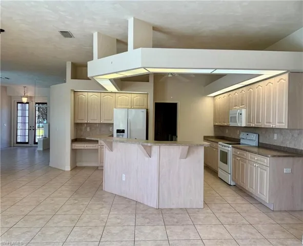 Kitchen with ceiling fan, a breakfast bar, light tile patterned floors and white appliances