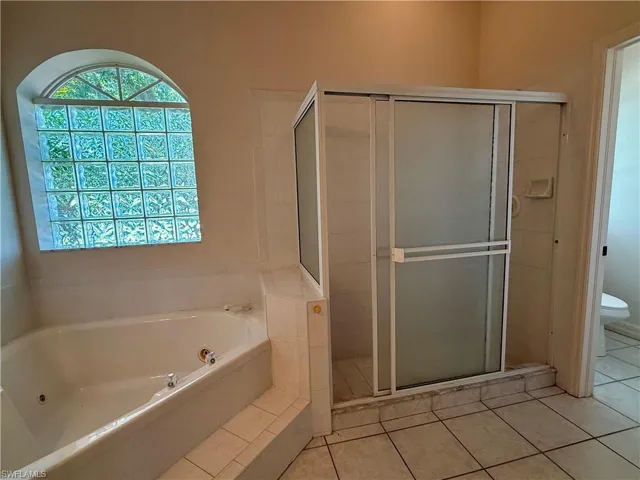 Bathroom featuring a tub with jets, tile patterned flooring, a stall shower, and toilet.