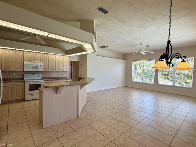 Kitchen with decorative backsplash, ceiling fan with chandelier, light tile patterned floors, and white appliances.
