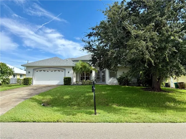 View of front facade with driveway, stucco siding, a garage, a front lawn, and french doors