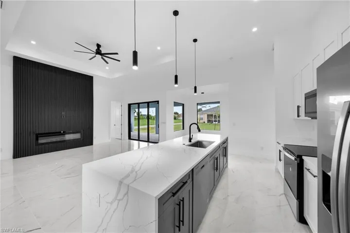 Kitchen with a center island with sink, appliances with stainless steel finishes, sink, ceiling fan, and a raised ceiling