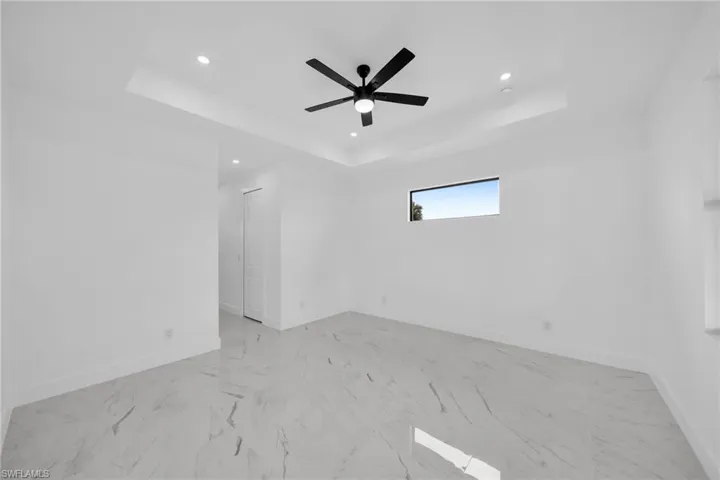 Tiled empty room with ceiling fan and a raised ceiling
