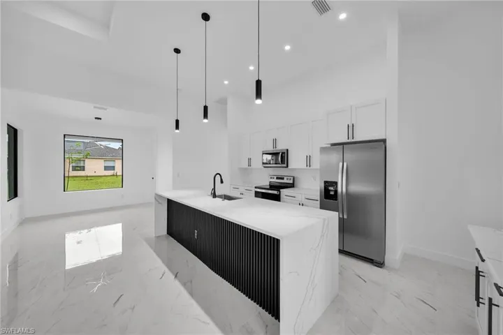 Kitchen with decorative light fixtures, white cabinets, a kitchen island with sink, appliances with stainless steel finishes, and light tile floors