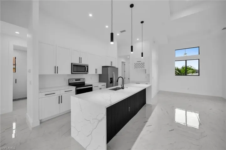 Kitchen with a towering ceiling, hanging light fixtures, an island with sink, white cabinets, and appliances with stainless steel finishes