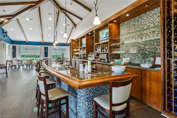 Bar with dark wood-type flooring, decorative light fixtures, a community bar, and vaulted ceiling with beams
