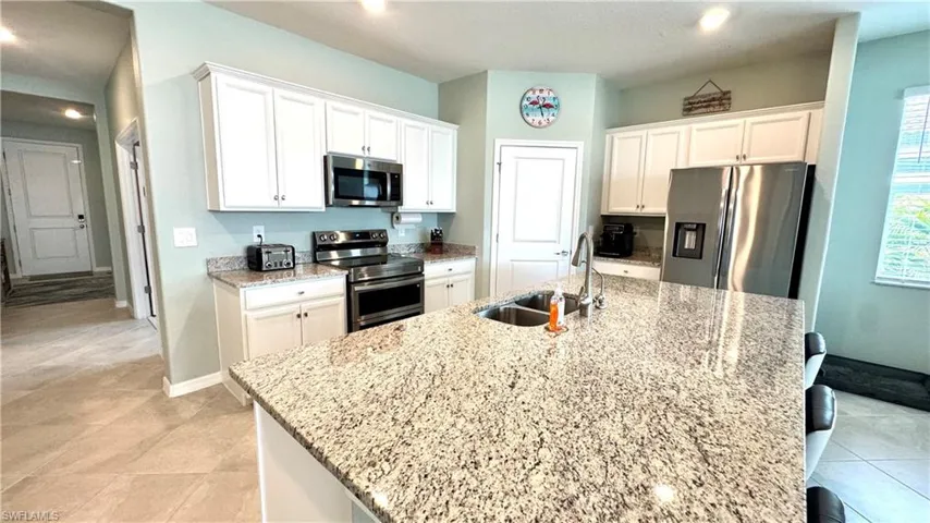 Kitchen with sink, white cabinetry, stainless steel appliances, light stone countertops, and an island with sink