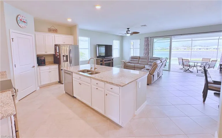 Kitchen featuring sink, light stone counters, appliances with stainless steel finishes, a kitchen island with sink, and white cabinets
