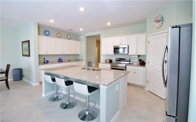 Kitchen with sink, white cabinets, light stone counters, stainless steel appliances, and a center island with sink