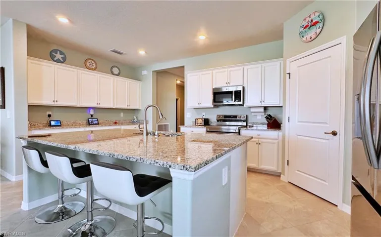 Kitchen featuring white cabinetry, sink, stainless steel appliances, light stone countertops, and a center island with sink