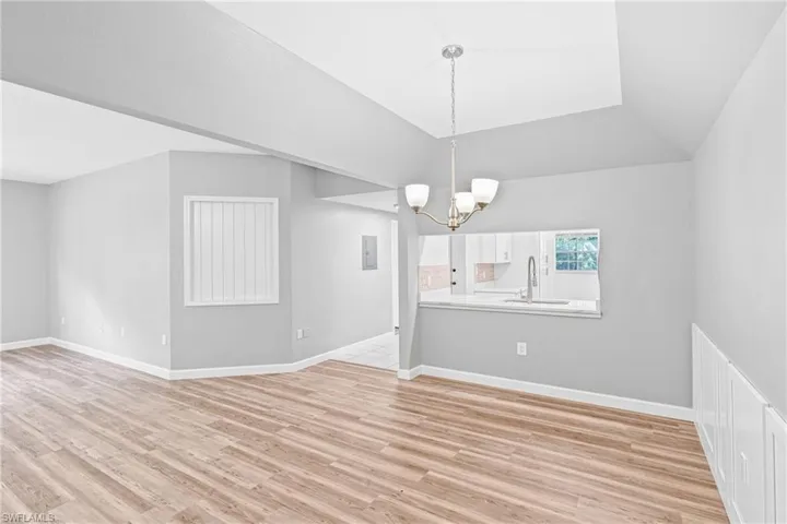 Unfurnished dining area with a chandelier, light wood-style flooring, vaulted ceiling, and electric panel