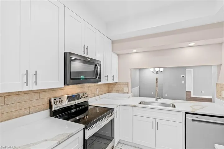 Kitchen with appliances with stainless steel finishes, white cabinets, light stone counters, tasteful backsplash, and recessed lighting