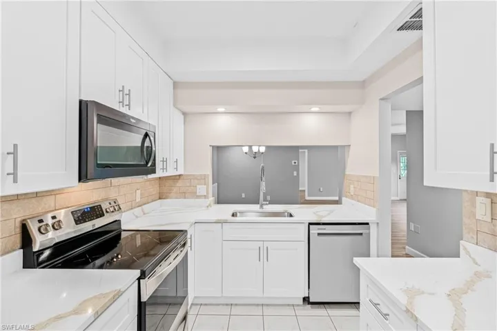 Kitchen with appliances with stainless steel finishes, decorative backsplash, light stone counters, and white cabinetry