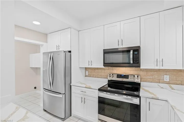 Kitchen featuring appliances with stainless steel finishes, white cabinets, tasteful backsplash, light stone counters, and recessed lighting