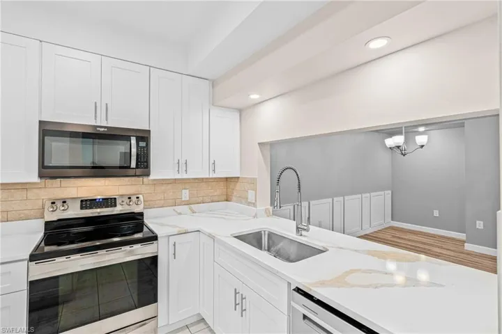 Kitchen featuring appliances with stainless steel finishes, backsplash, recessed lighting, white cabinets, and light stone countertops