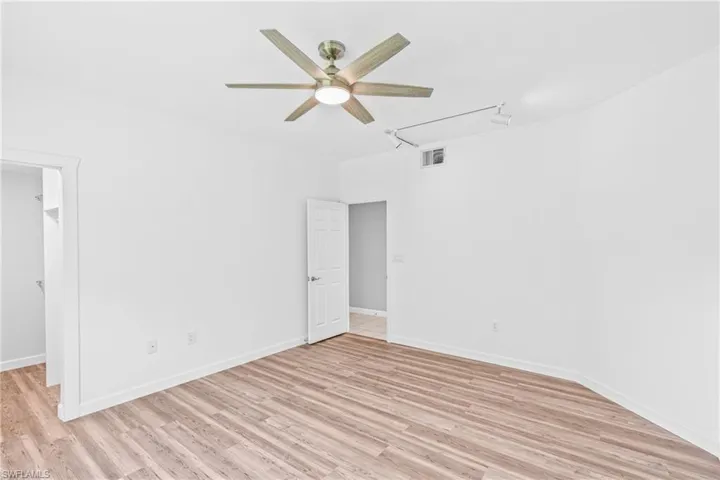 Unfurnished bedroom featuring track lighting, attic access, a ceiling fan, light wood-style floors, and a walk in closet