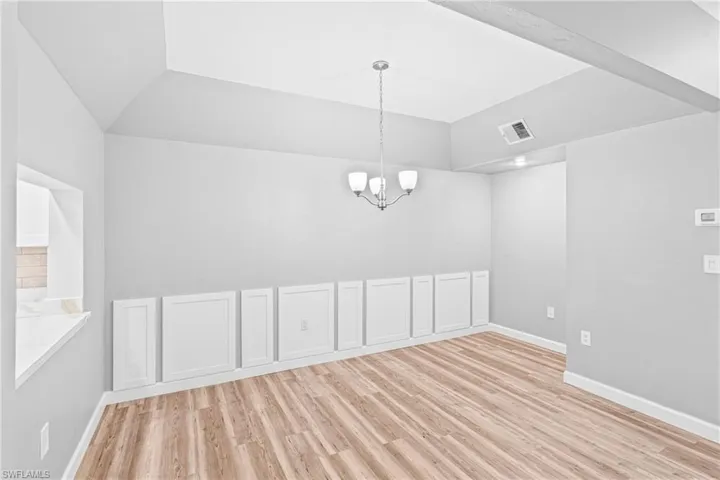 Unfurnished dining area with light wood-style flooring, vaulted ceiling, and a chandelier