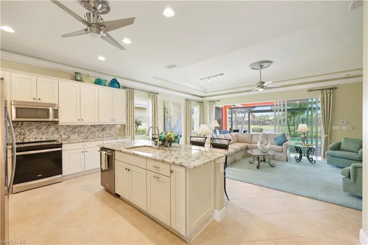 Kitchen with ceiling fan, crown molding, a tray ceiling, light tile patterned flooring, and open floor plan