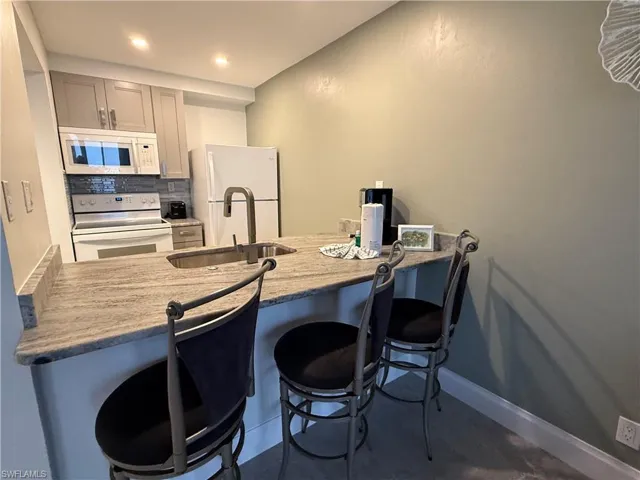 Kitchen featuring white appliances, gray cabinetry, sink, backsplash, and a breakfast bar