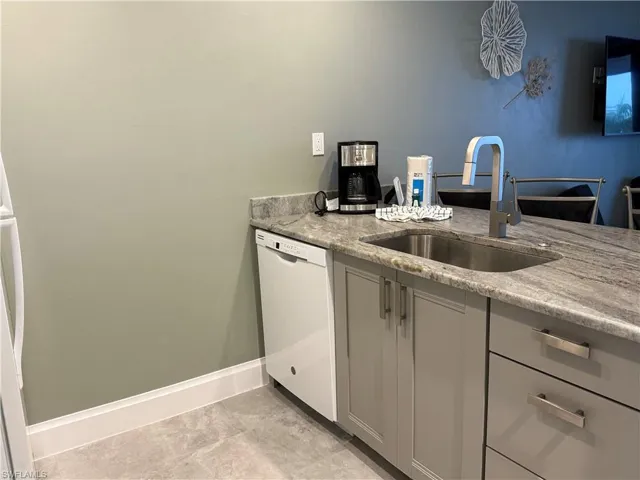 Kitchen with gray cabinetry, light stone counters, white dishwasher, and sink