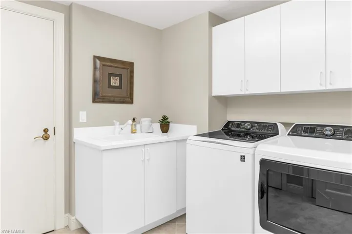Laundry room featuring washer and dryer, light tile patterned flooring, cabinets, and sink