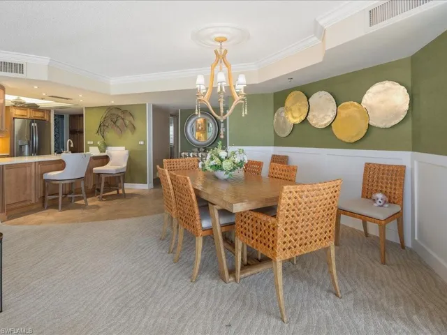 Dining area featuring crown molding, a raised ceiling, a chandelier, wainscoting, and a decorative wall