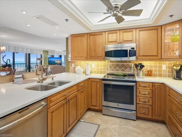 Kitchen featuring appliances with stainless steel finishes, light stone counters, a raised ceiling, brown cabinetry, and recessed lighting