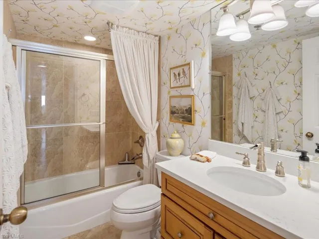 Bathroom with wallpapered walls, combined bath / shower with glass door, and vanity
