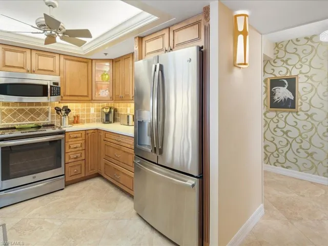 Kitchen with appliances with stainless steel finishes, ceiling fan, decorative backsplash, a tray ceiling, and wallpapered walls
