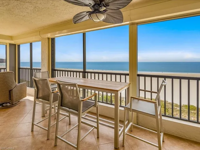 Sunroom with healthy amount of natural light, view of water and beach, a textured ceiling, and tile patterned floors