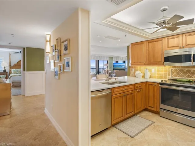 Kitchen with appliances with stainless steel finishes, tasteful backsplash, a ceiling fan, light stone counters, and brown cabinetry