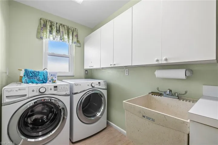 Laundry area featuring independent washer and dryer, sink, light wood-style floors, and cabinets