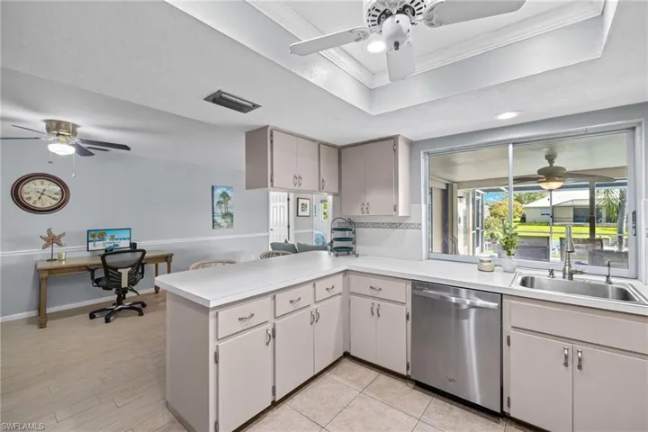 Kitchen with kitchen peninsula, dishwasher, ceiling fan, a raised ceiling, and sink